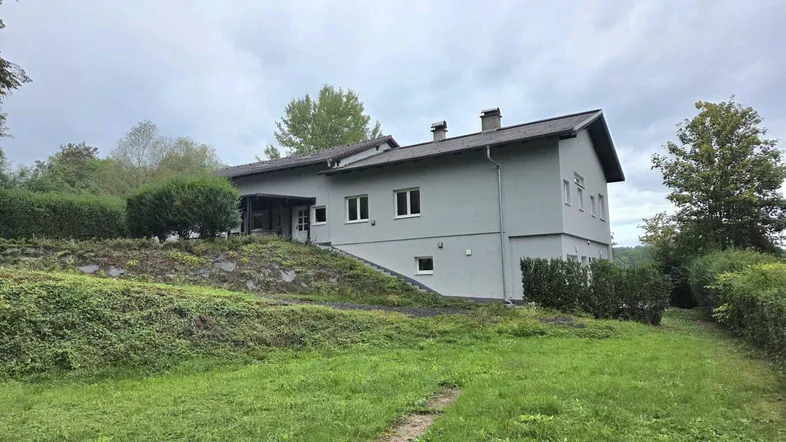 Graues Einfamilienhaus mit Satteldach und großem Gartenbereich unter bewölktem Himmel.