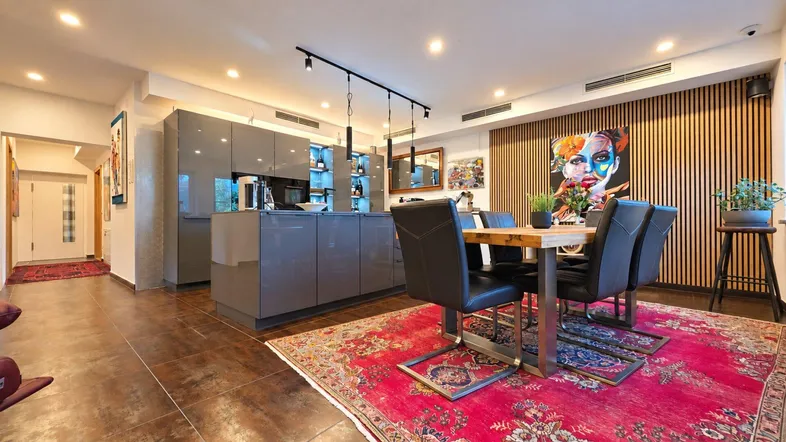 Moderne offene Küche und Essbereich mit Holzwandverkleidung und farbenfrohem Teppich.