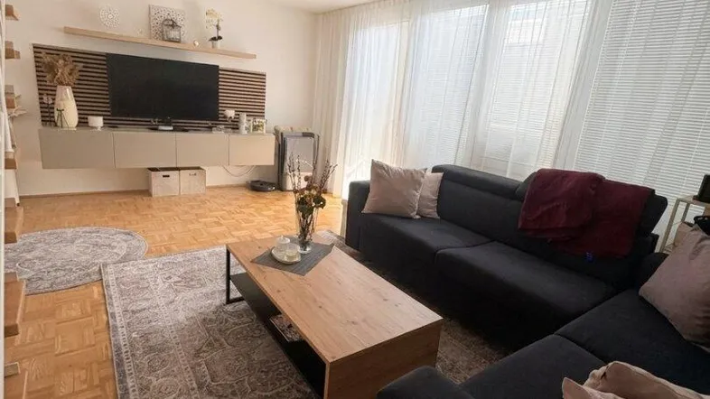 Helles Wohnzimmer mit Parkettboden, großem Sofa und modernem TV-Möbel an der Wand.