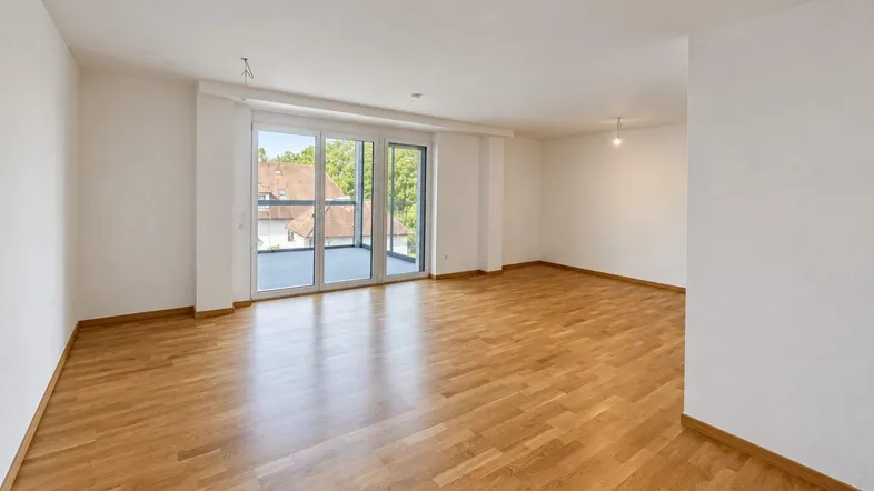 Helles Wohnzimmer mit Parkettboden und Zugang zu einem großen Balkon mit Blick ins Grüne.
