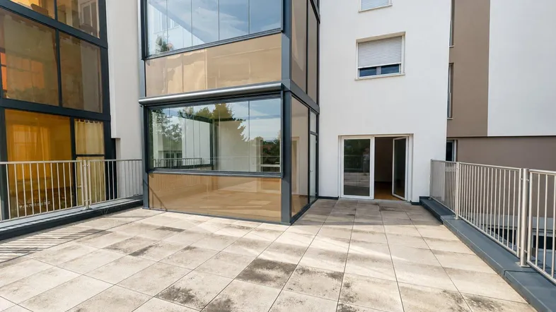Große geflieste Terrasse mit Glasanbau und Zugang zu den Innenräumen eines modernen Gebäudes.
