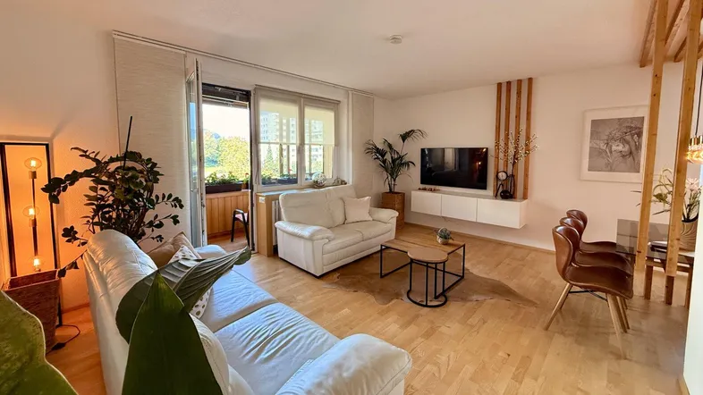 Helles Wohn- und Esszimmer mit Parkettboden, weißen Sofas und Zugang zum Balkon.
