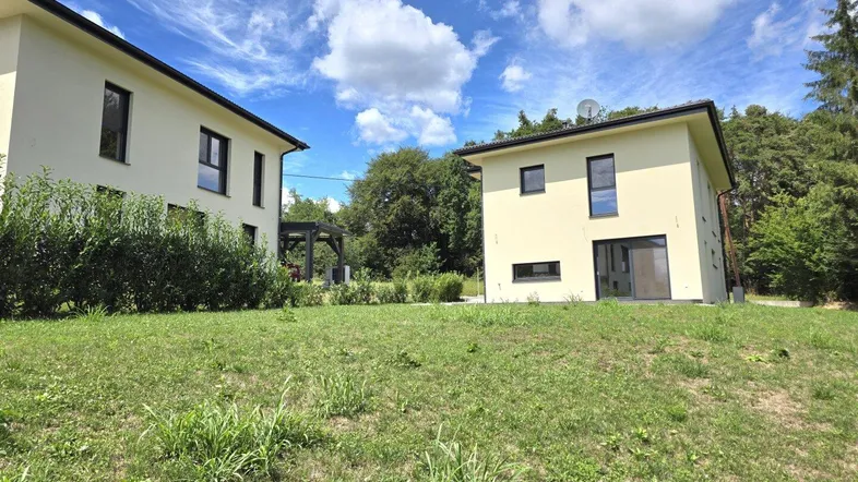 Zwei moderne Häuser mit heller Fassade und großem Gartenbereich unter blauem Himmel.
