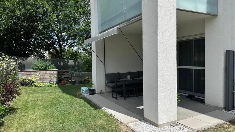 Moderne Terrasse mit Gartenmöbeln und angrenzendem Rasenbereich, umgeben von viel Grün.