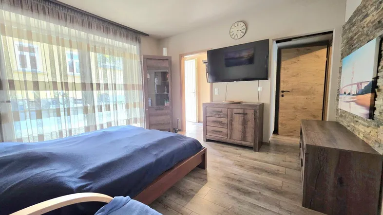 Helles Schlafzimmer mit Holzboden, großem Bett und einem Fernseher an der Wand.