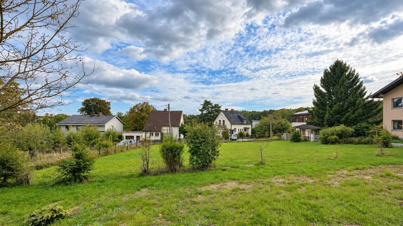 Grünes Grundstück mit umliegenden Häusern und Bäumen unter bewölktem Himmel.