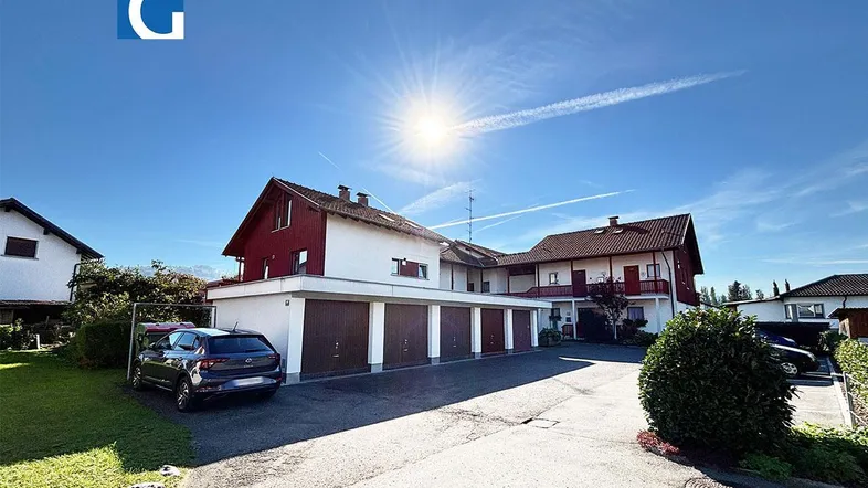 Mehrfamilienhaus mit Garagen und sonniger Auffahrt unter blauem Himmel.