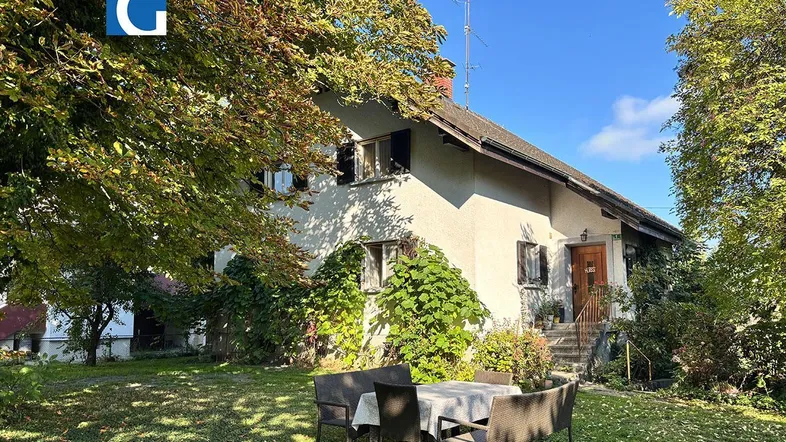 Charmantes Einfamilienhaus mit gepflegtem Garten und gemütlichem Sitzbereich unter Bäumen.