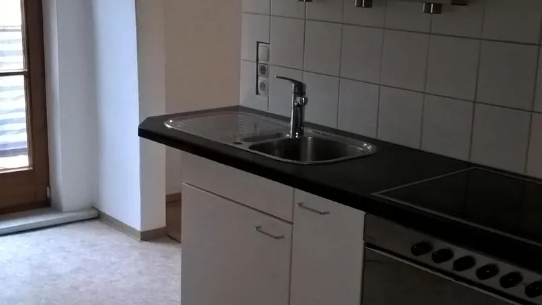 Helle Küche mit weißen Schränken, Spüle und Kochfeld, bereit für die Installation weiterer Geräte.