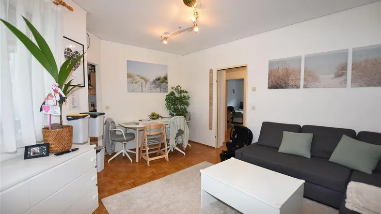 Gemütlicher Wohn-Essbereich mit Parkettboden, Sofa und Esstisch, ideal für Familienleben.