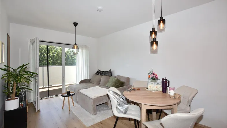 Helles Wohn- und Esszimmer mit Holzboden, Zugang zum Balkon und moderner Beleuchtung.