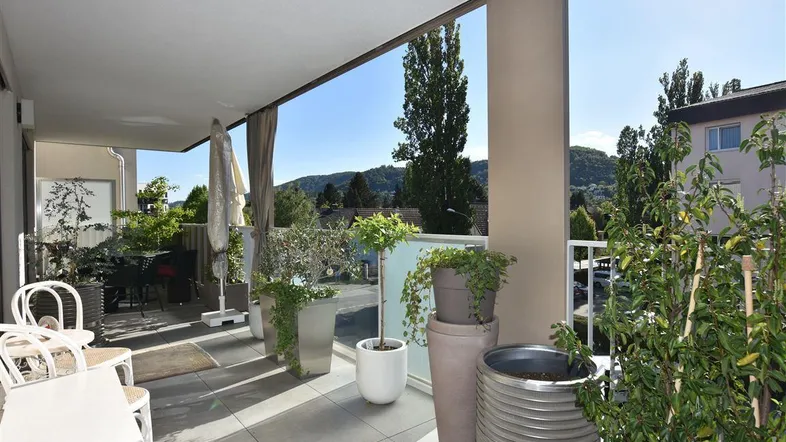 Geräumiger Balkon mit Fliesenboden, Pflanzen und Sitzgelegenheiten, bietet einen weiten Blick ins Grüne.