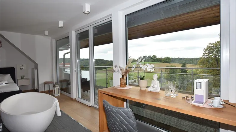 Geräumiges Schlafzimmer mit freistehender Badewanne, Holzboden und Zugang zu einem Balkon mit Landschaftsblick.