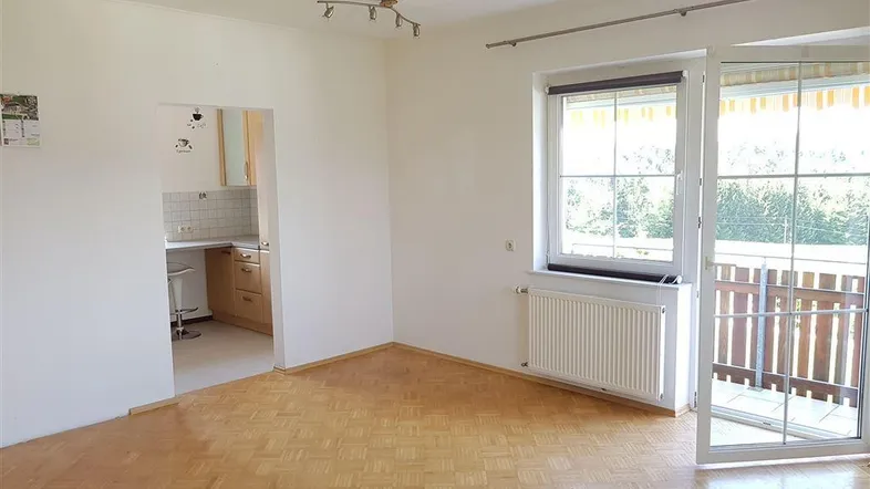 Helles Wohnzimmer mit Parkettboden und Zugang zum Balkon, angrenzend an eine Küche.