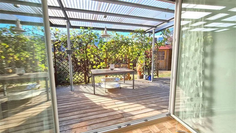 Heller Innenraum mit Zugang zu einer überdachten Holzterrasse und Blick ins Grüne.