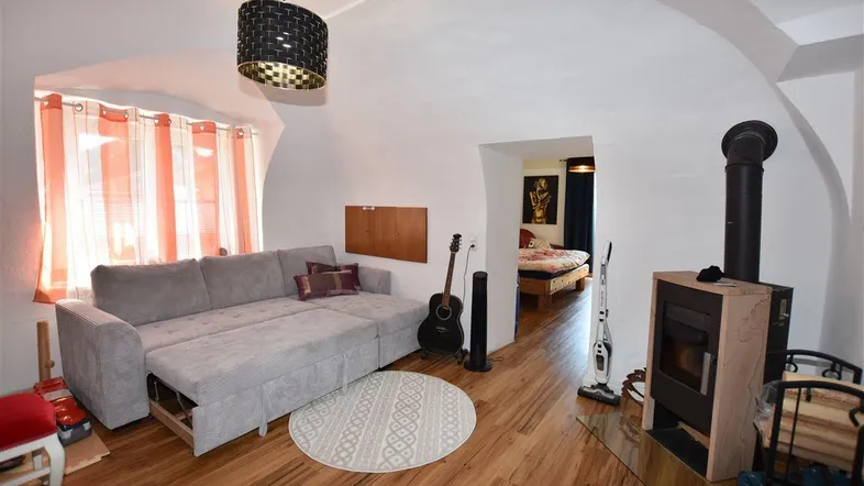 Gemütliches Wohnzimmer mit Holzboden, Kaminofen und Zugang zu einem Schlafbereich.