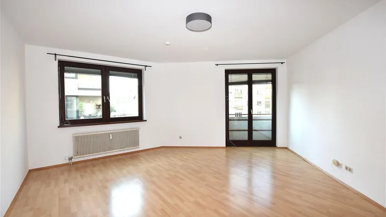 Helles Zimmer mit Parkettboden, weißen Wänden und Zugang zu einem Balkon oder einer Terrasse.