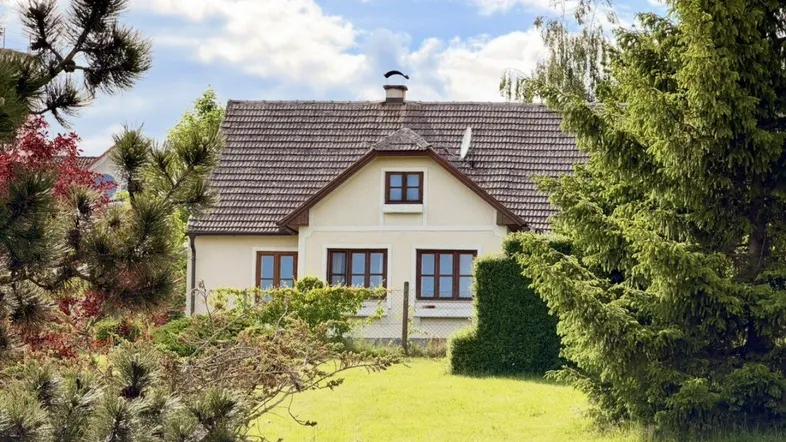 Traditionelles Einfamilienhaus mit Satteldach und gepflegtem Garten umgeben von Bäumen.