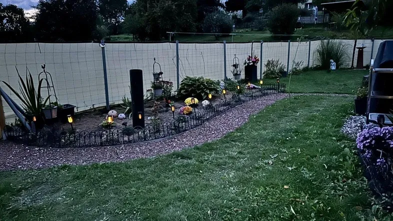 Gepflegter Gartenbereich mit dekorativer Beleuchtung und Kiesweg am Abend, umgeben von Grün.