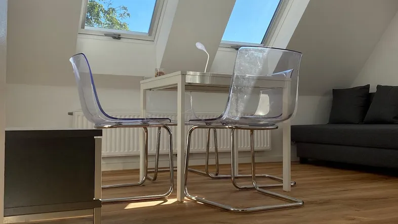 Helles Dachgeschosszimmer mit Holzboden, modernen Stühlen und zwei großen Dachfenstern, die viel Licht hereinlassen.