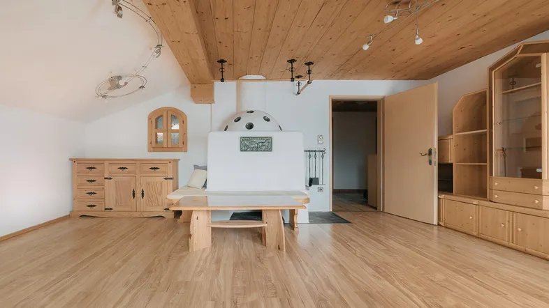 Geräumiges Wohnzimmer im alpinen Stil mit Holzbalkendecke, Kachelofen und hellem Laminatboden.