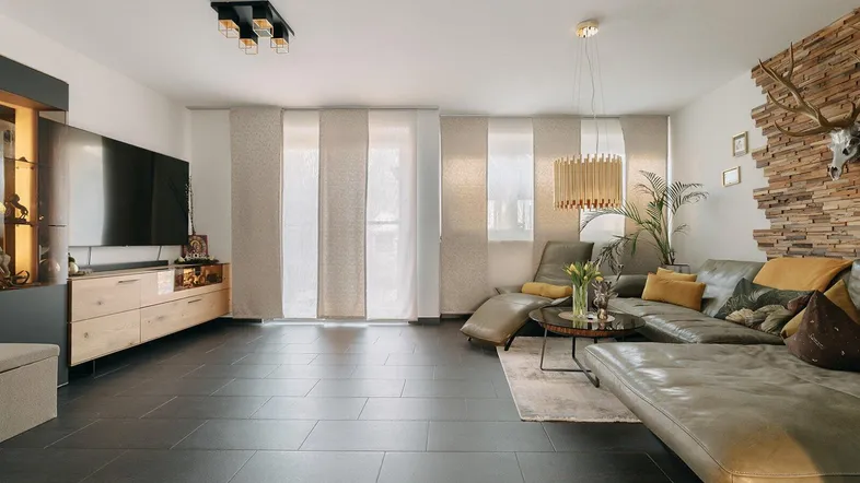 Geräumiges Wohnzimmer mit dunklen Fliesen, bequemer Couch und dekorativer Holzwand.