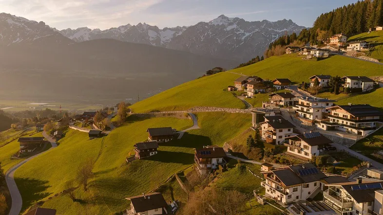 Idyllische Wohnsiedlung auf einem sonnigen Berghang mit atemberaubendem Panorama der umliegenden Alpenlandschaft.