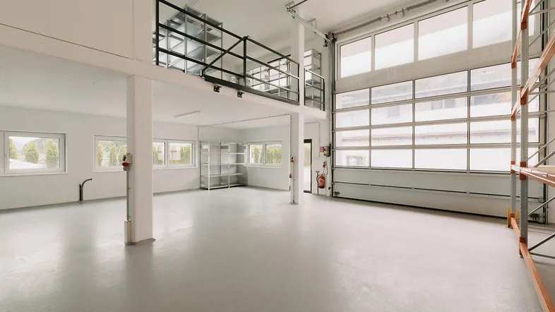 Geräumige Lagerhalle mit hohen Decken, Betonboden und einem Zwischengeschoss für zusätzliche Fläche.