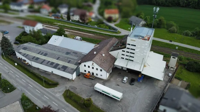 Luftaufnahme eines Industrie- oder Gewerbekomplexes mit mehreren Gebäuden und angrenzenden Bahngleisen in ländlicher Umgebung.