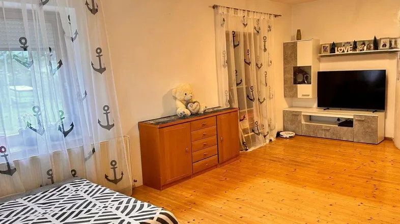 Helles Wohnzimmer mit Holzboden, Anker-Vorhängen und einem TV-Möbel.