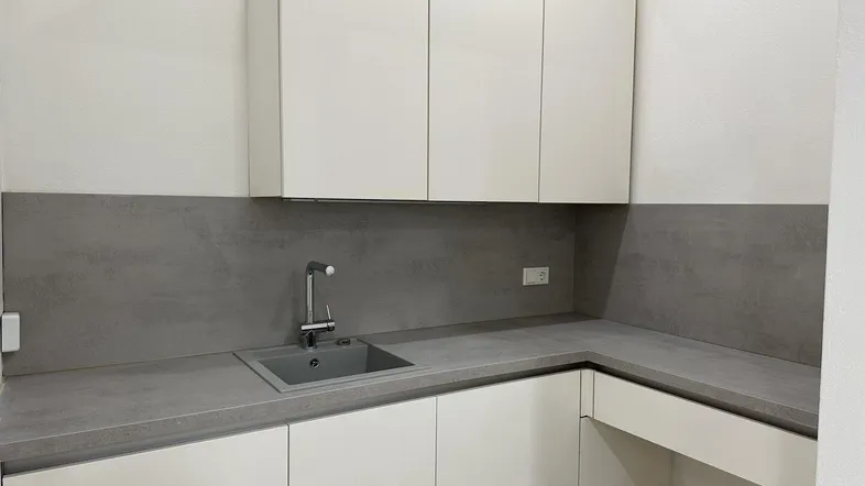 Moderne Küchenzeile mit weißen Schränken, grauer Arbeitsplatte und integriertem Spülbecken.