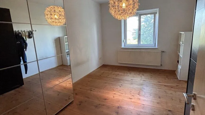 Helles Schlafzimmer mit Holzdielenboden, großem Spiegelschrank und dekorativer Deckenleuchte.