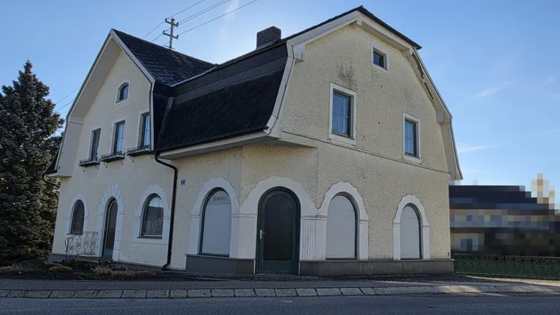 Traditionelles Gebäude mit heller Fassade und Mansarddach unter blauem Himmel.