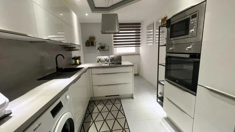 Moderne Küche mit weißen Hochglanzfronten, integrierten Geräten und Waschmaschine.