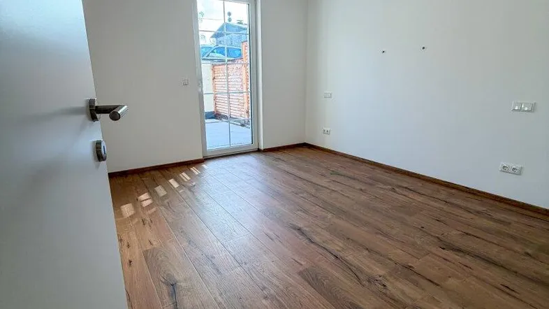 Helles Zimmer mit Holzboden und Zugang zu einer kleinen Terrasse oder Balkon.