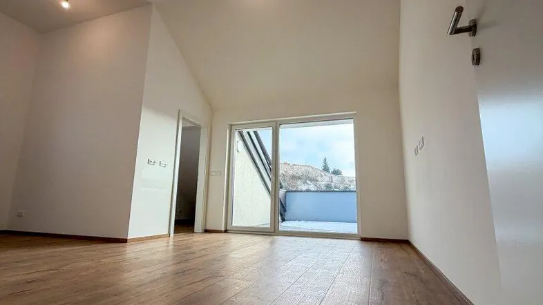 Geräumiger Wohnbereich mit hohen Decken, Holzboden und Zugang zu einem Balkon.