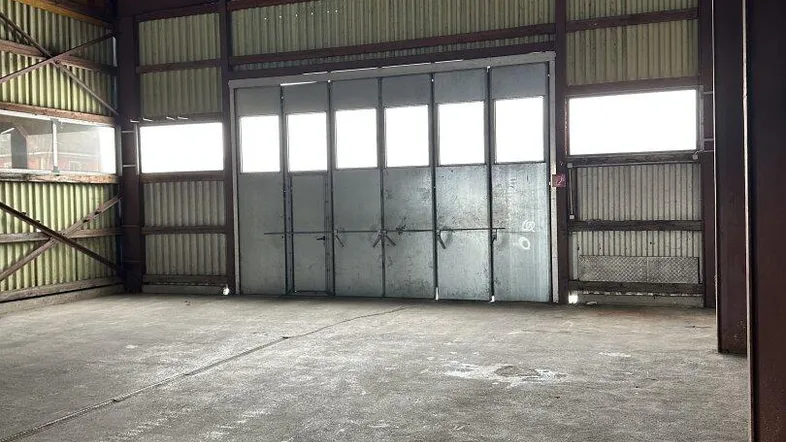Geräumige Lagerhalle mit hohen Decken, Betonboden und großem Rolltor für den Zugang.