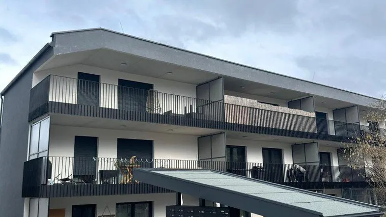 Modernes Mehrfamilienhaus mit dunkler Fassade, Balkonen und einem überdachten Eingangsbereich.