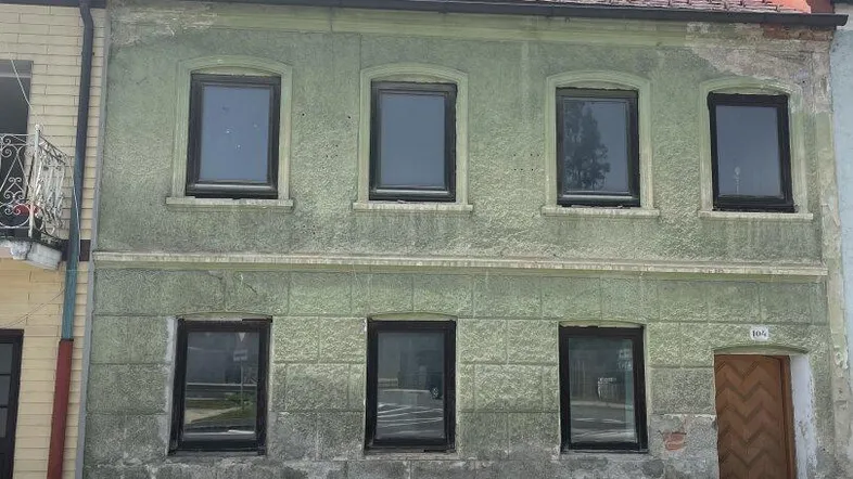 Altes Wohnhaus mit verputzter Fassade in hellem Grün und braunem Ziegeldach.