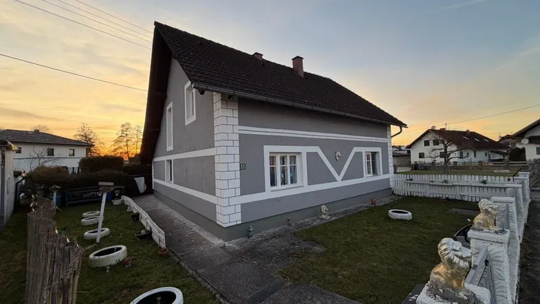 Graues Einfamilienhaus mit weiß abgesetzten Fassadendetails und Vorgarten bei Sonnenuntergang.