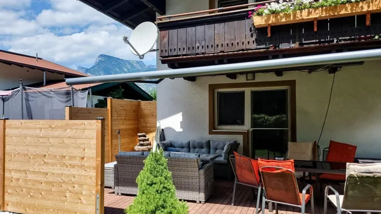 Gemütliche Terrasse mit Gartenmöbeln, Sonnenschutz und Blick auf die Berge.