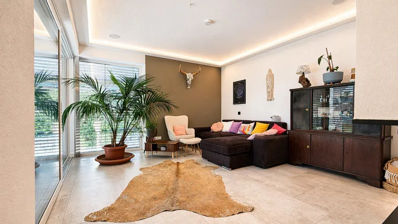 Geräumiges Wohnzimmer mit großem Sofa, Fliesenboden und Zugang zur Terrasse.