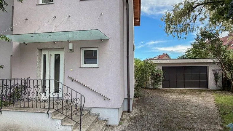 Vorderansicht eines Hauses mit Eingangsbereich, Treppe und einer langen Auffahrt zur Garage.