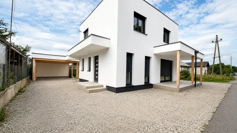 Freistehendes modernes Haus mit weißer Fassade, Carport und großzügiger Kiesauffahrt.