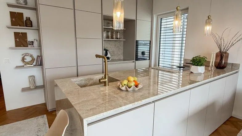 Moderne Küche mit Kücheninsel, Marmorarbeitsplatte und eleganten Pendelleuchten für stilvolles Kochen.