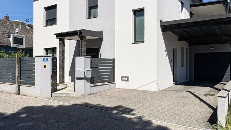 Modernes Einfamilienhaus mit heller Fassade, Carport und gepflasterter Einfahrt.