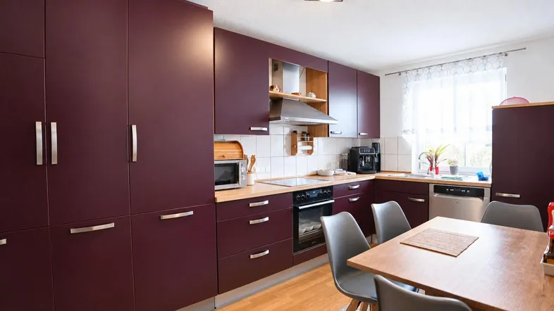 Moderne Einbauküche in dunklem Rot mit Holzboden und Essbereich am Fenster.