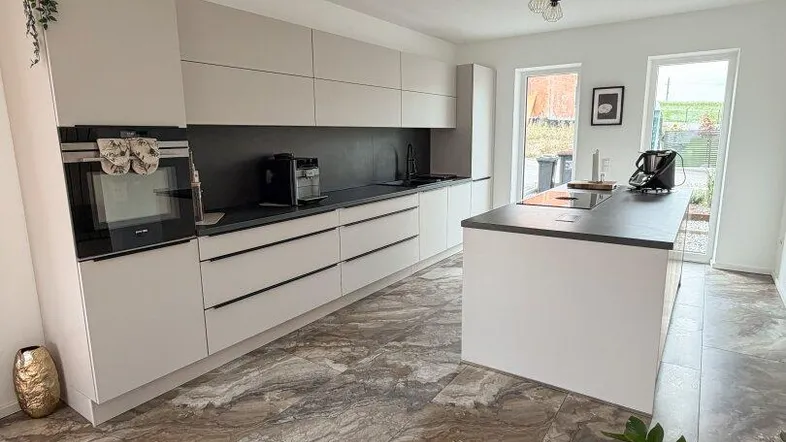 Moderne Küche mit Kücheninsel, hellen Schränken, dunklen Arbeitsplatten und gemustertem Fliesenboden.