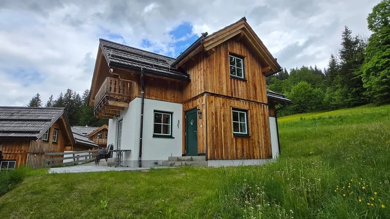 Traditionelles Holzhaus im alpinen Stil mit Satteldach und Balkon, umgeben von grünen Wiesen.