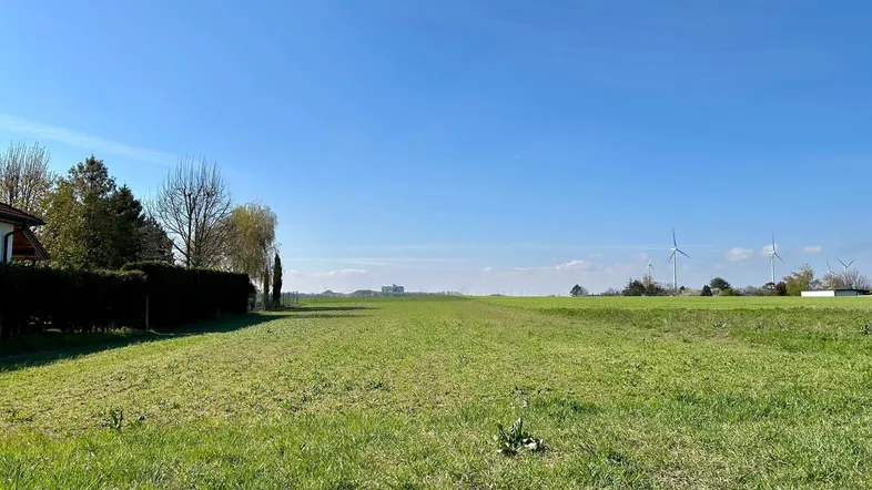 Weitläufiges grünes Feld unter klarem blauem Himmel mit Windrädern am Horizont.